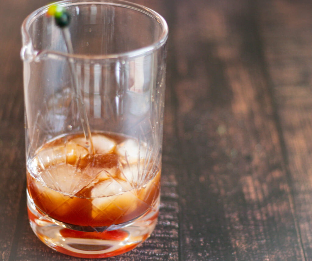 An image of a semi tall glass with red vermouth mix and ice of a cocktail called Negroni